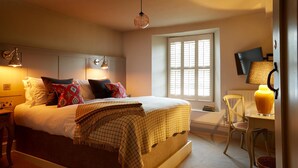 A bedroom with a bed, bedside lamps, a window, a desk, and a chair. - The Bull Hotel (Fairford)