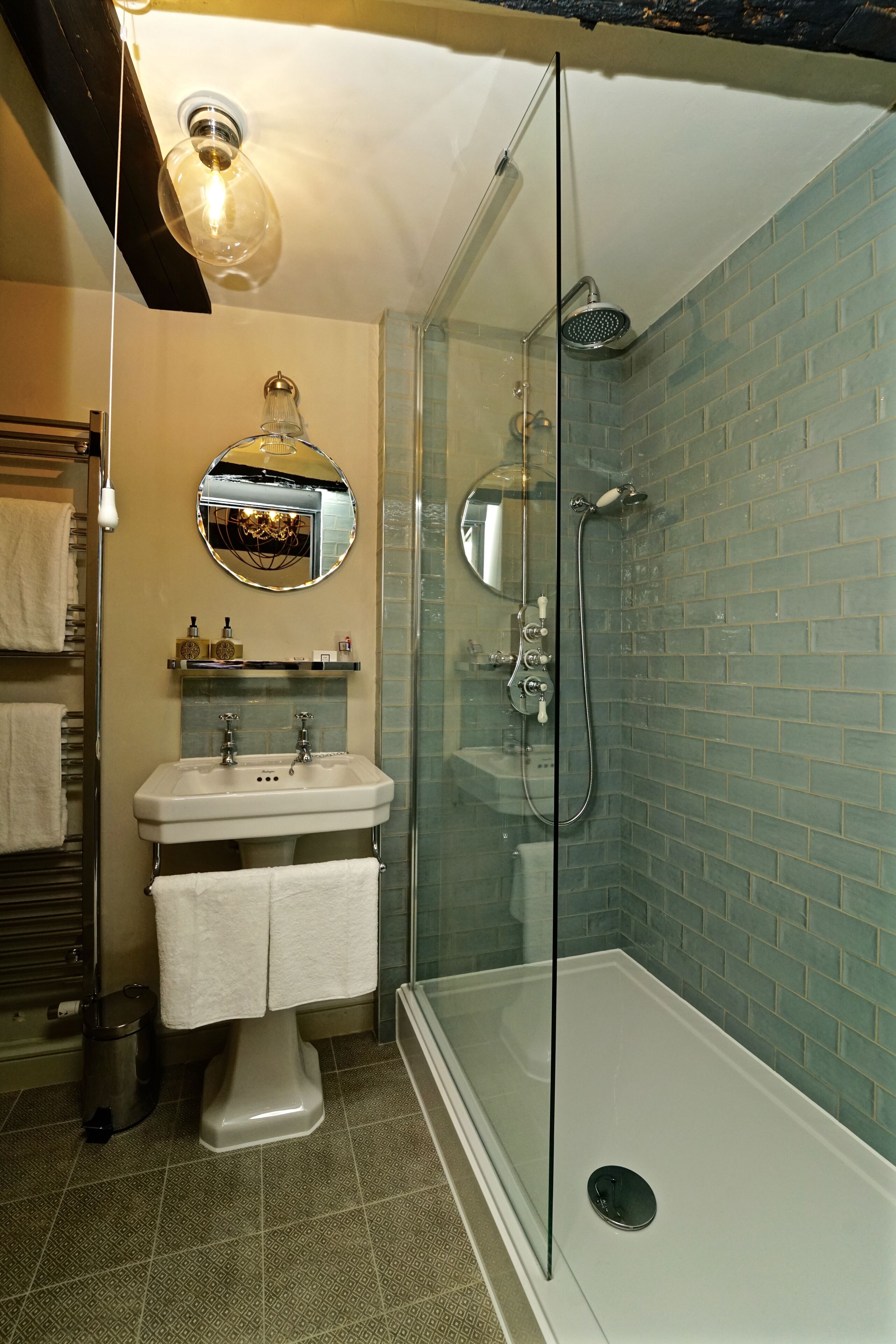 Een badkamer met een douche met glazen wand, een wastafel met spiegel erboven en een handdoekrek met handdoeken.