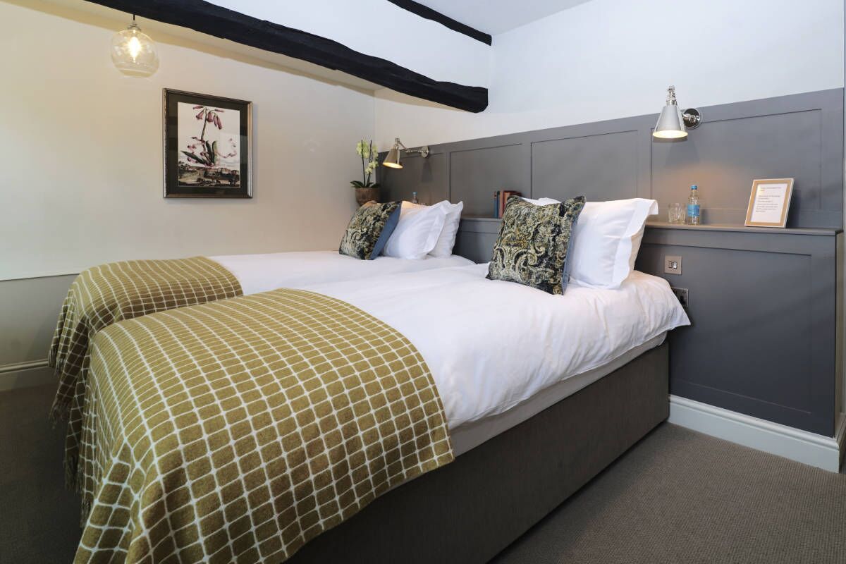 A double bed with a checkered bedspread, two bedside tables with lamps, a framed picture on the wall, and a grey headboard.
