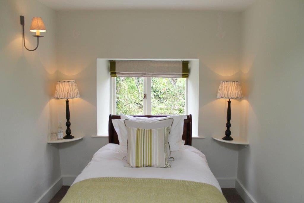 Een netjes ingerichte slaapkamer met een bed centraal geplaatst tussen twee nachtkastjes, elk met een lamp. Achter het bed is een raam te zien met uitzicht op groen.