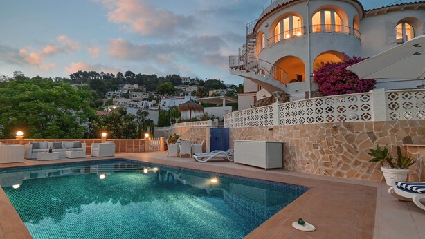 A pool area with a clear blue pool, white lounge chairs, and a stone wall with a decorative pattern.