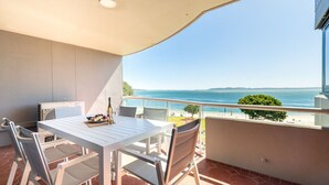 A balcony with a table set for two, overlooking a beach and the sea. - Florentine, 14/11 Columbia Cl - – AIRCON, WIFI, UNSURPASSED WATER VIEWS (Nelson Bay)