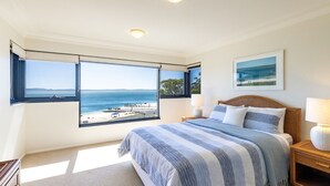 A bedroom with a large window offering a view of the sea and a pier. - Florentine, 14/11 Columbia Cl - – AIRCON, WIFI, UNSURPASSED WATER VIEWS (Nelson Bay)