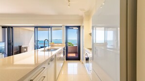 A modern kitchen with a large island, a view of the sea, and a sliding door leading to a balcony. - Florentine, 14/11 Columbia Cl - – AIRCON, WIFI, UNSURPASSED WATER VIEWS (Nelson Bay)
