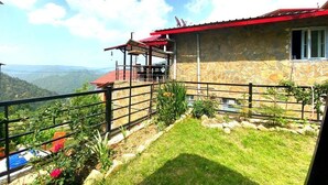 Un bâtiment en pierre avec un toit rouge, une terrasse entourée d’une clôture et une vue sur les montagnes.