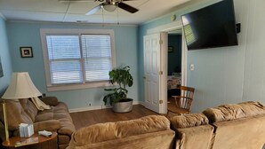 A living room with a brown sofa, a lamp, a potted plant, and a television mounted on the wall. - House: Lower  prices! Snowbirds Welcome!  Bring your boat for fall fishing (Beaufort)