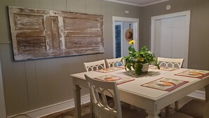 A dining area with a white table set for four, surrounded by white chairs. A large rustic painting hangs on the wall above the table. - House: Lower  prices! Snowbirds Welcome!  Bring your boat for fall fishing (Beaufort)