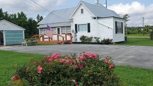 A white single-story house with a porch, an American flag, and a small garden with pink flowers. - House: Lower  prices! Snowbirds Welcome!  Bring your boat for fall fishing (Beaufort)