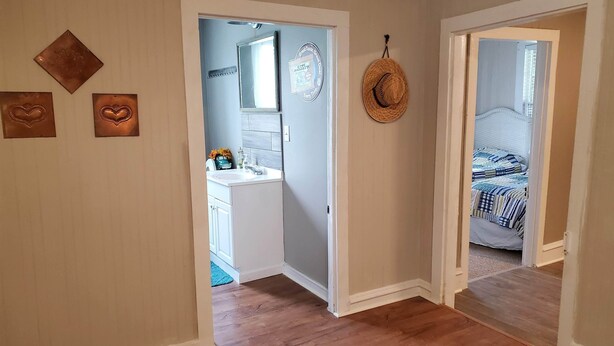 A hallway with wooden flooring, a bathroom with a sink and mirror, and a bedroom with a bed. - House: Lower  prices! Snowbirds Welcome!  Bring your boat for fall fishing (Beaufort)