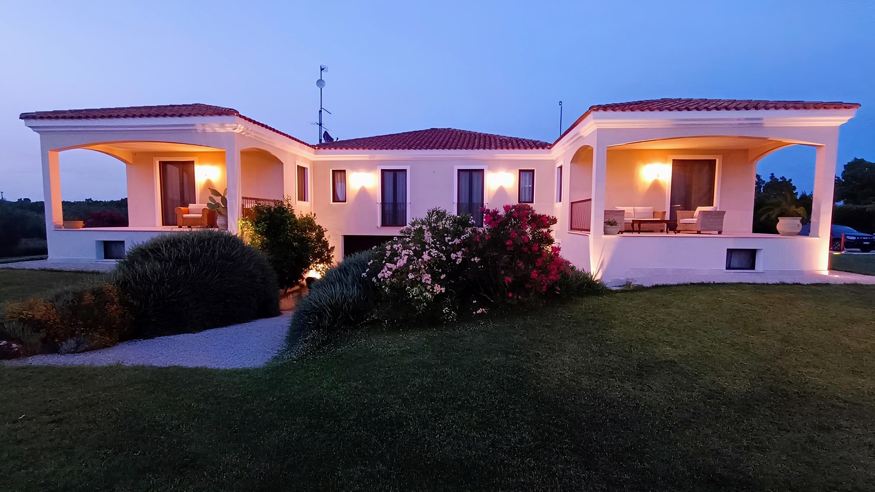 A two-story house with a covered patio area, a well-maintained lawn, and a variety of flowering plants.