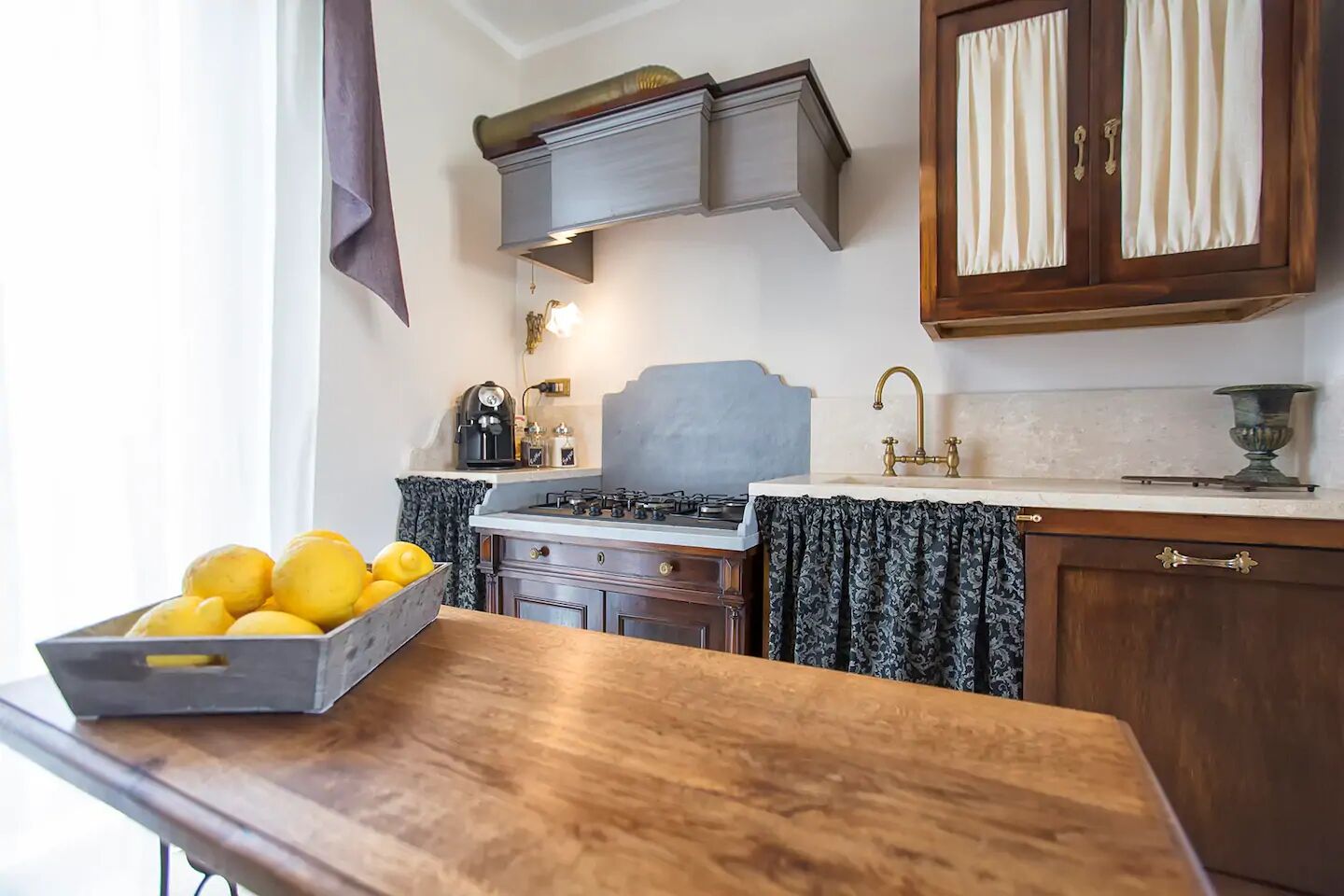 A kitchen with a gas stove, a coffee maker, and a bowl of lemons on the counter.