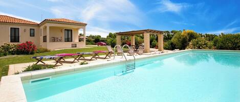 Une piscine avec des chaises longues et une pergola.