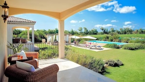 Eine überdachte Terrasse mit Korbmöbeln, einem Pool und Blick auf die Landschaft.
