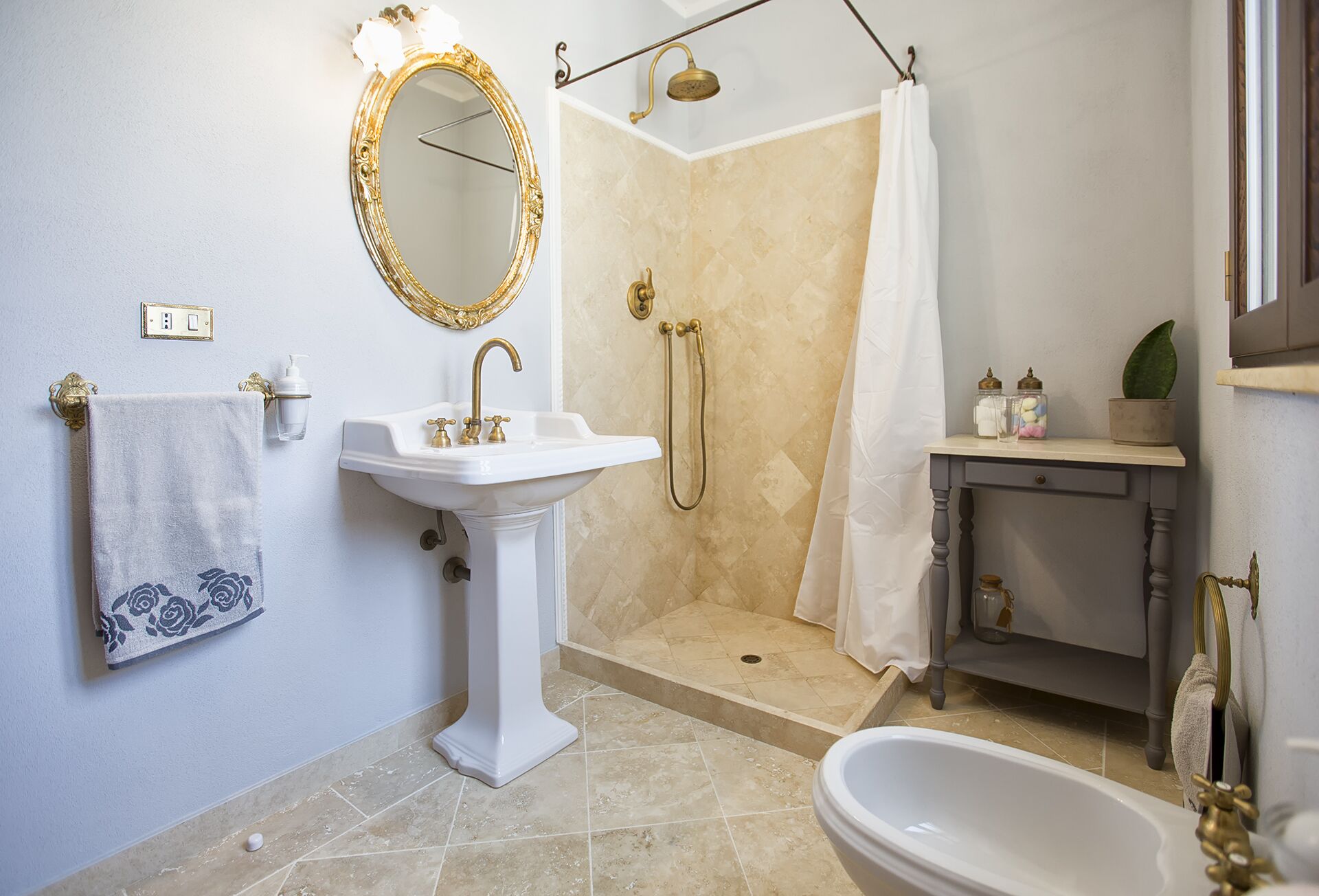 Une salle de bain avec un lavabo sur colonne, une baignoire îlot, une douche avec une porte en verre et un meuble-lavabo avec un miroir et des étagères.