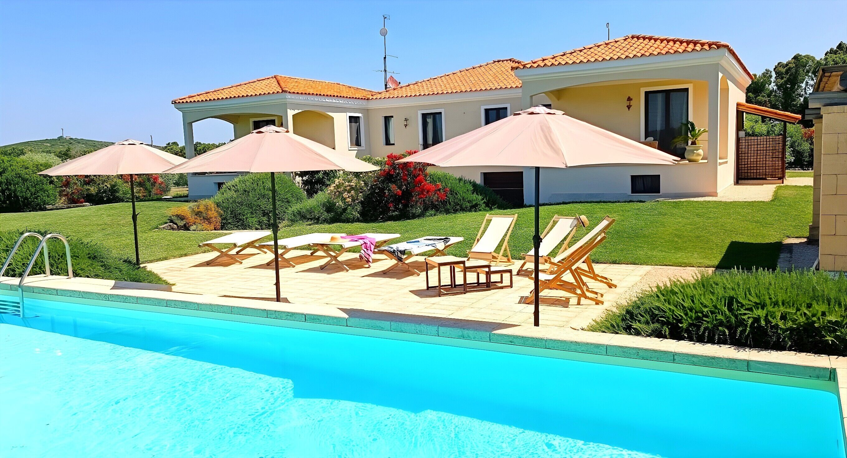 Une piscine avec des chaises longues et des parasols, une maison avec un toit en tuiles et une pelouse bien entretenue.