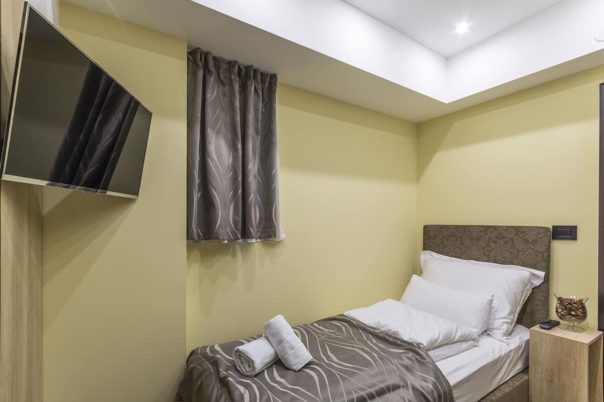 A neatly made bed with white linens, a folded towel, and a small bedside table with a glass bowl and a remote control.