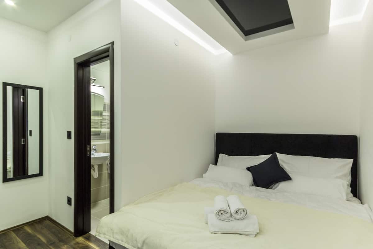 A hotel room with a bed, a bathroom visible through an open door, and a mirror on the wall.