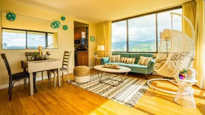 A spacious living room with a large window, a dining area, and a cozy seating area with a hanging chair.