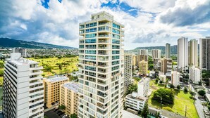 A high-rise building with multiple balconies, surrounded by other buildings and a park.