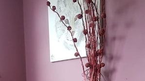 Eine Ecke mit einem Holzschrank, einer weißen Vase mit roten Zweigen und einem gerahmten Bild an der Wand.
