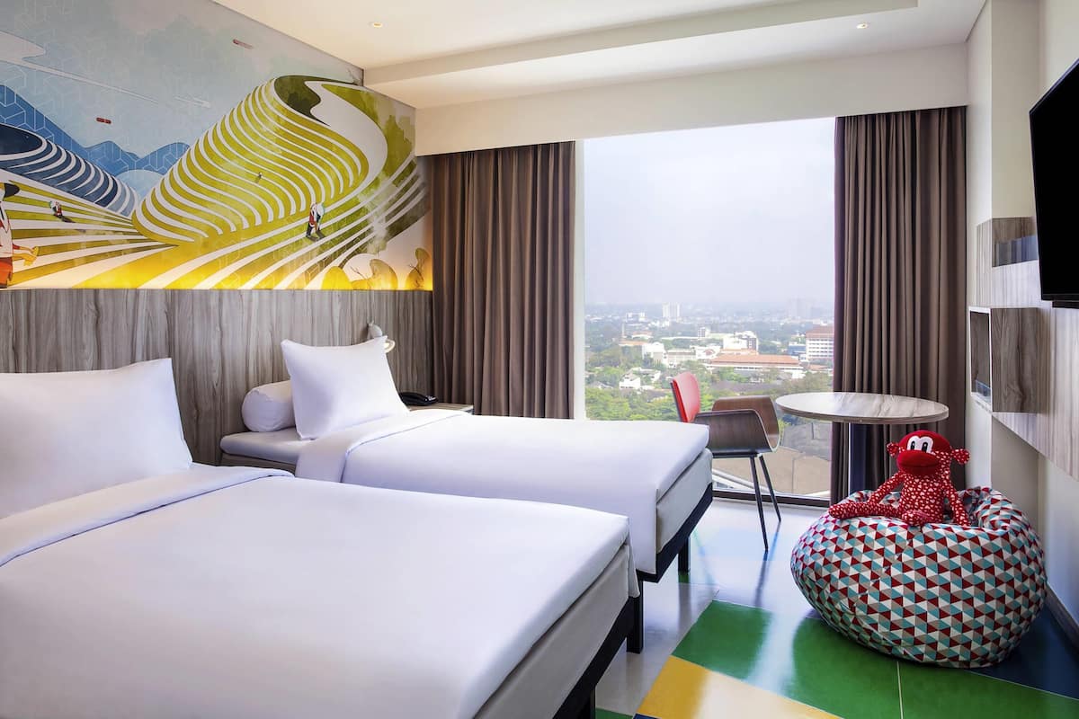 A hotel room with two beds, a city view, a round table, and a colorful bean bag.