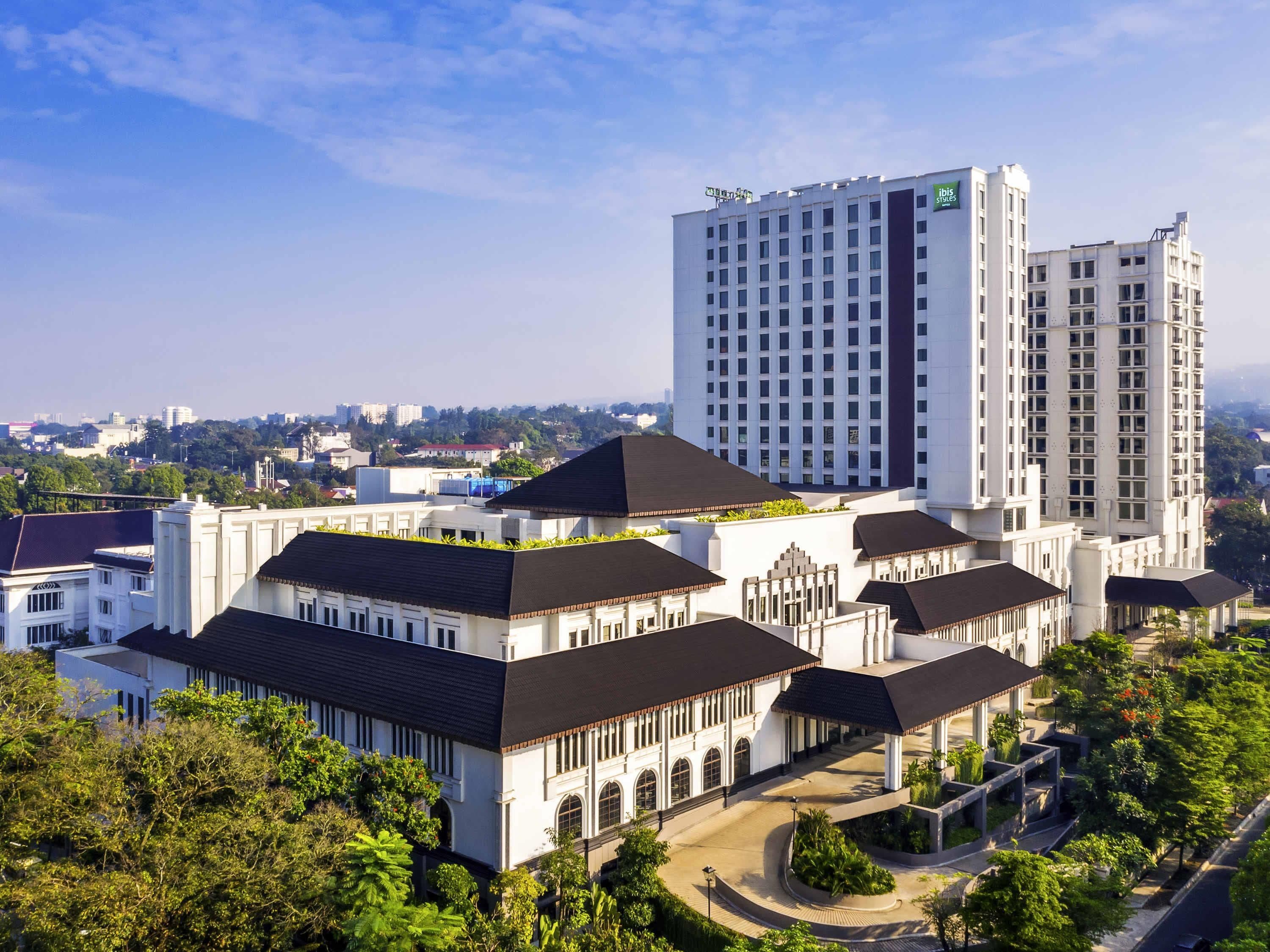 A modern hotel with a central courtyard, surrounded by lush greenery and a view of a cityscape in the background.