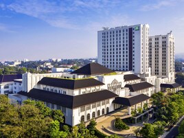 Ett modernt hotell med en central innergård, omgivet av frodig grönska och med utsikt över en stadssiluett i bakgrunden.