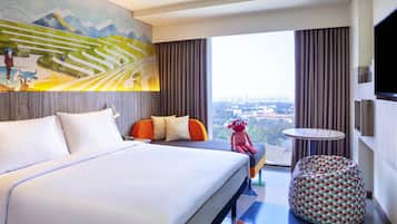 A modern hotel room with a large bed, a small round table, a bean bag chair, and a city view.