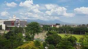 A view of a large building with a prominent sign for Telkom Indonesia, surrounded by lush greenery and a distant mountain range. - ibis Styles Bandung Grand Central (Bandung)