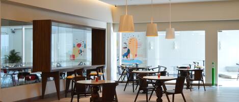 A modern restaurant with wooden tables and chairs, pendant lighting, and a large window with a view.