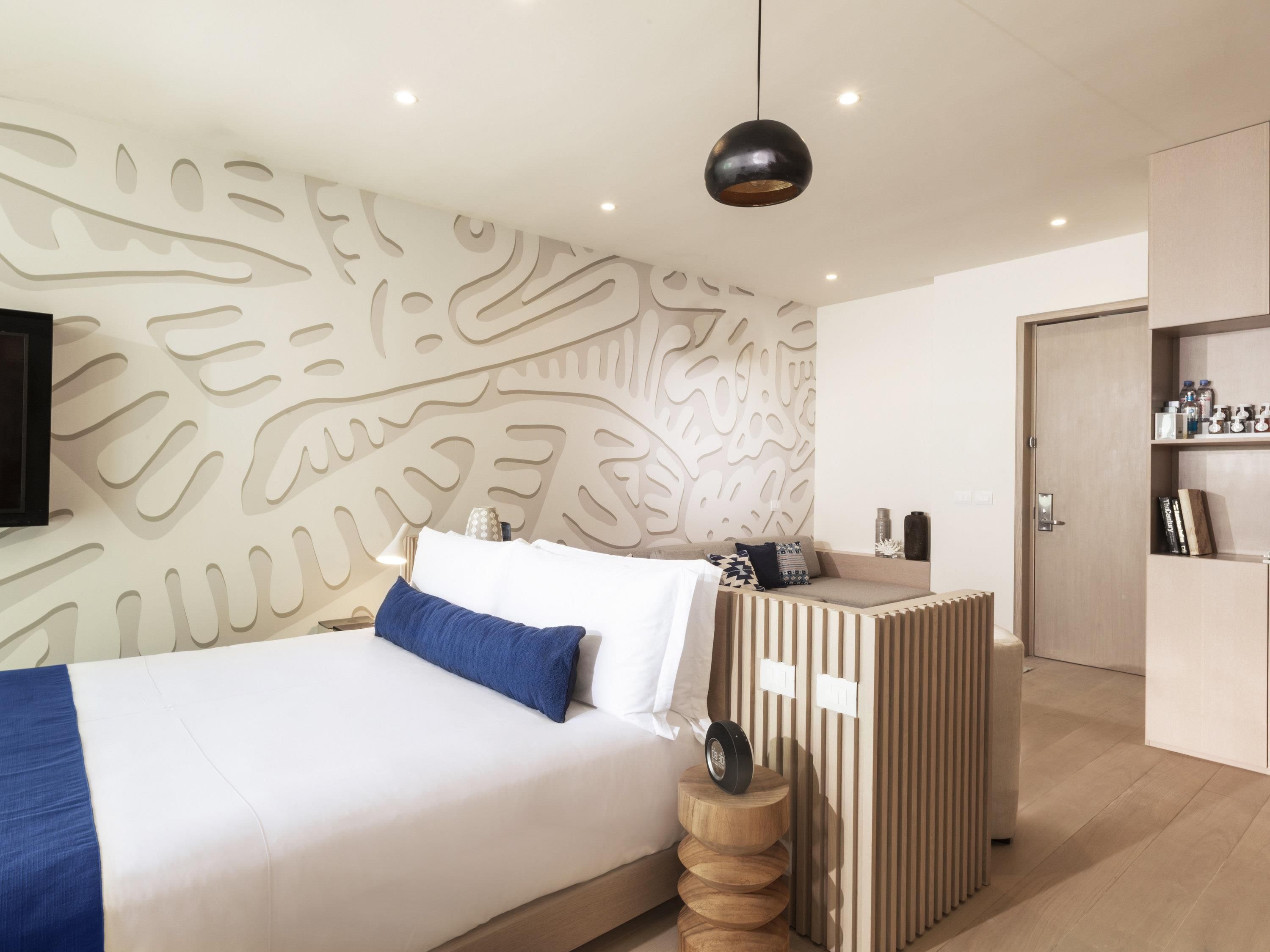 A modern bedroom with a bed, a wall with a leaf pattern, a bedside table, and a wardrobe.
