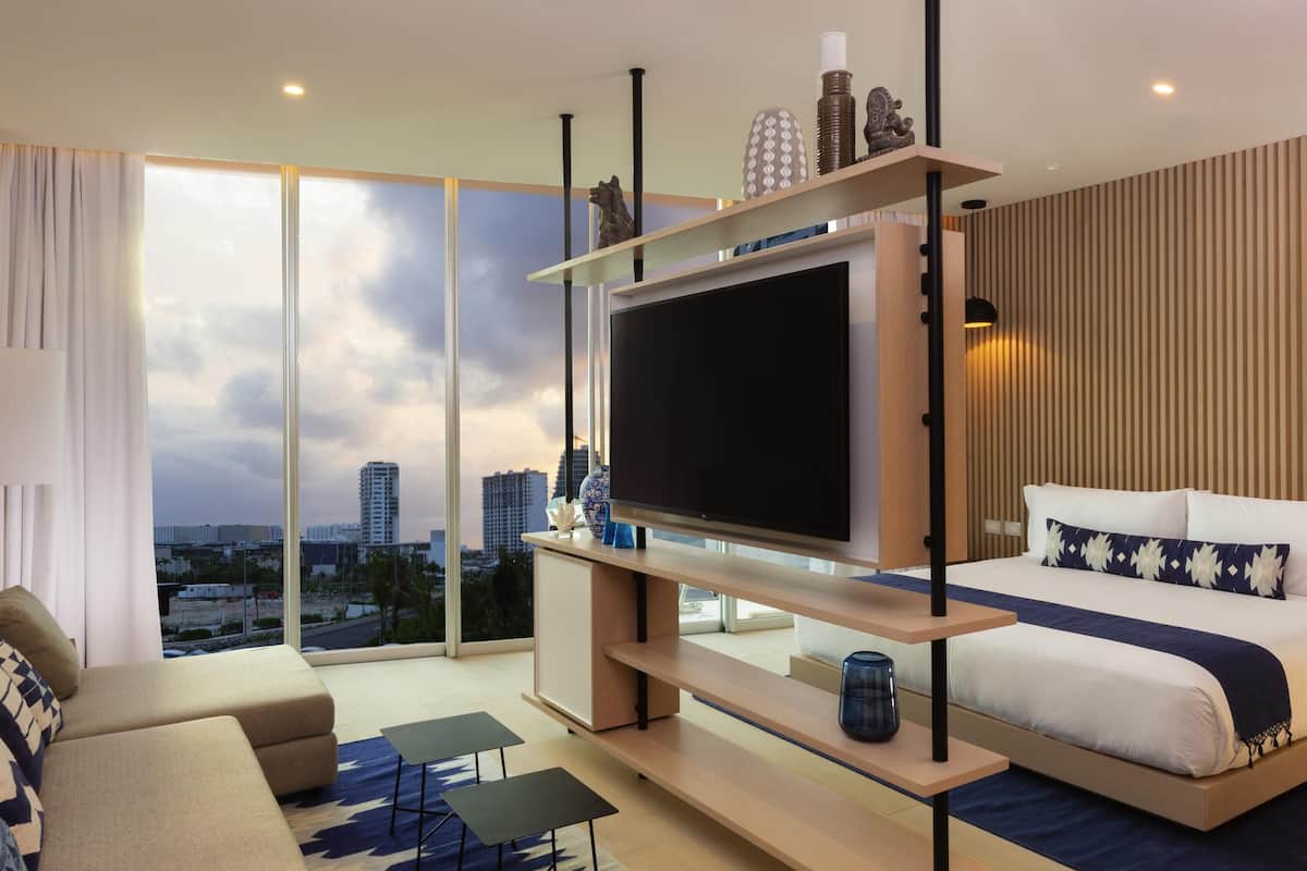 Ein modernes Hotelzimmer mit großem Fernseher, einem Bett, einer Couch und Blick auf die Stadt.