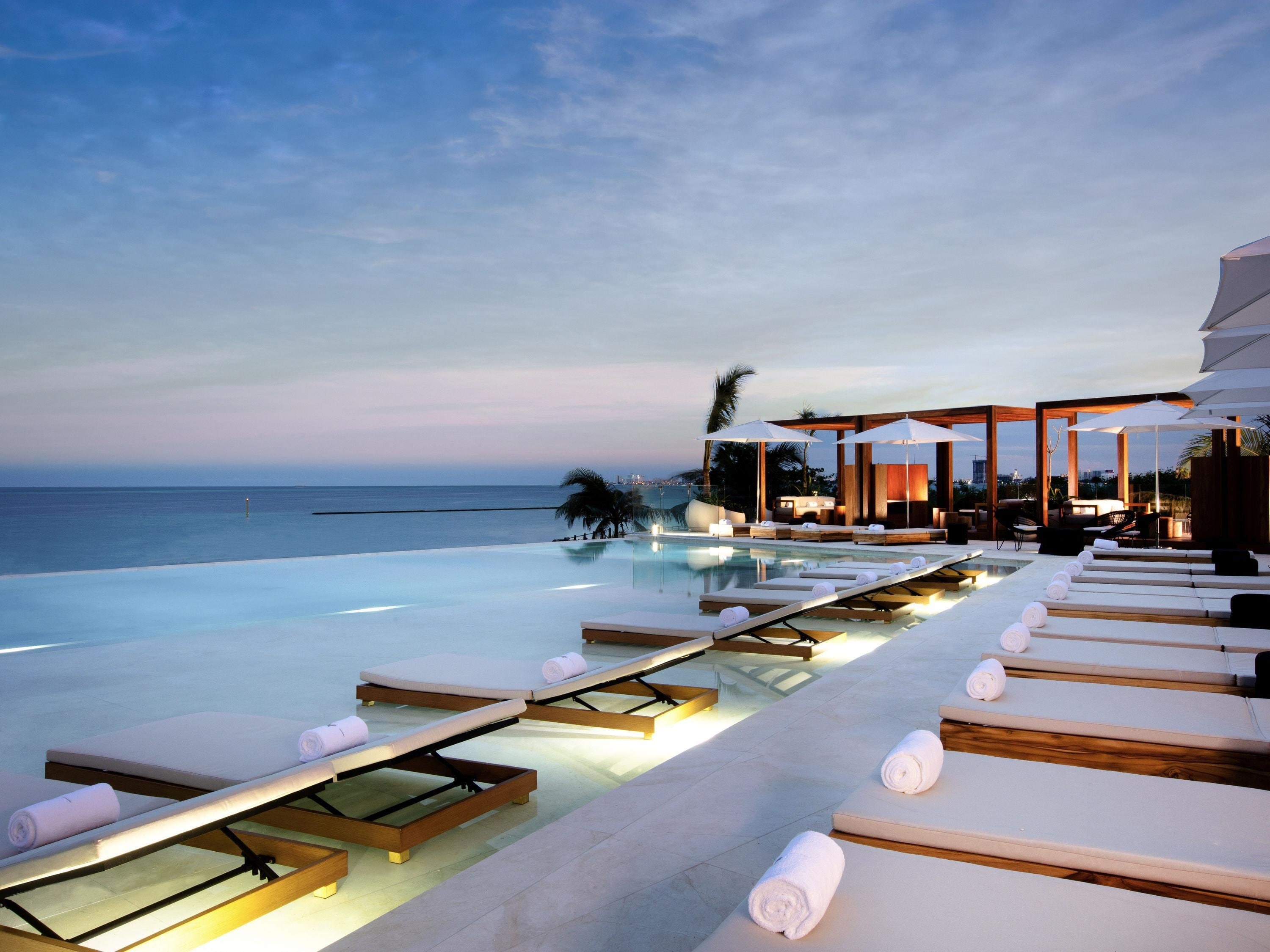 Piscina infinita con sillas de descanso y sombrillas, con vista al mar.