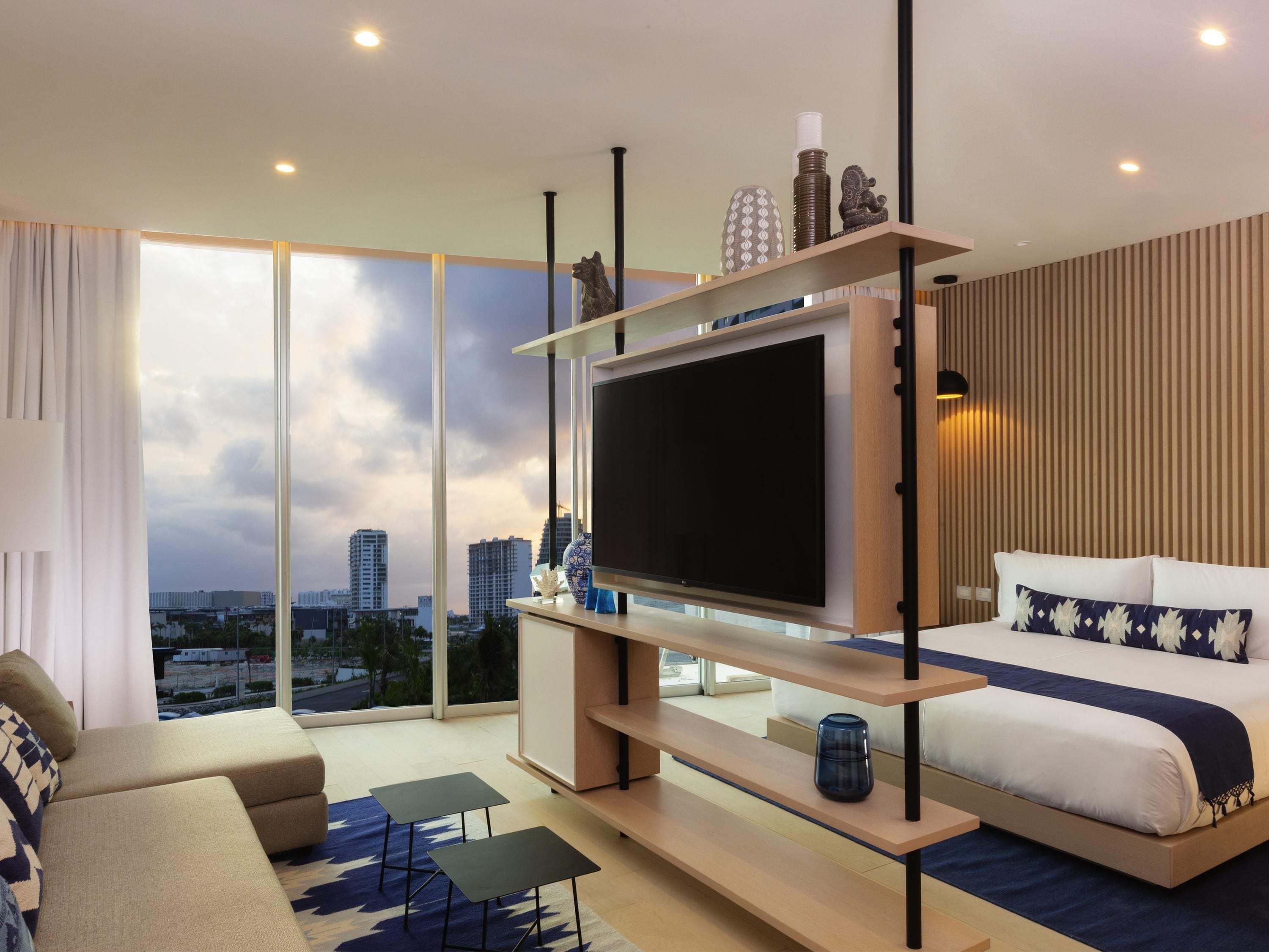 Una habitación de hotel moderna con un televisor grande, una cama, un sofá y vistas a la ciudad.