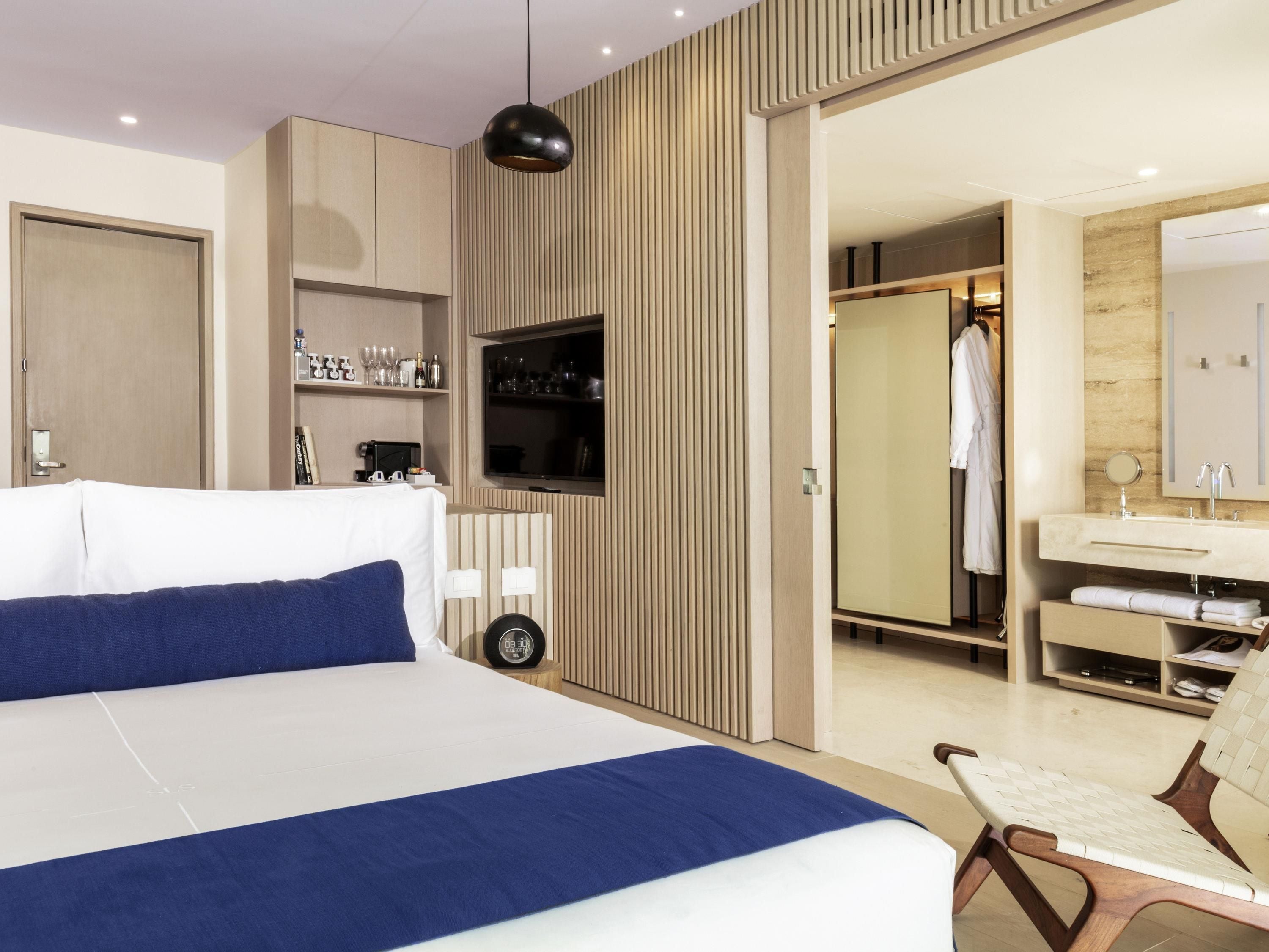 Ett modernt hotellrum med en stor säng, en TV, en garderob och ett badrum med spegel och handfat.