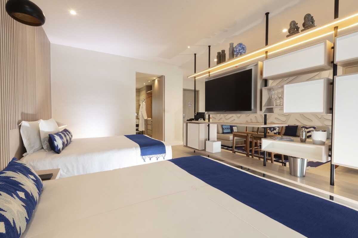 A modern hotel room with two beds, a desk, a TV, and a minibar.