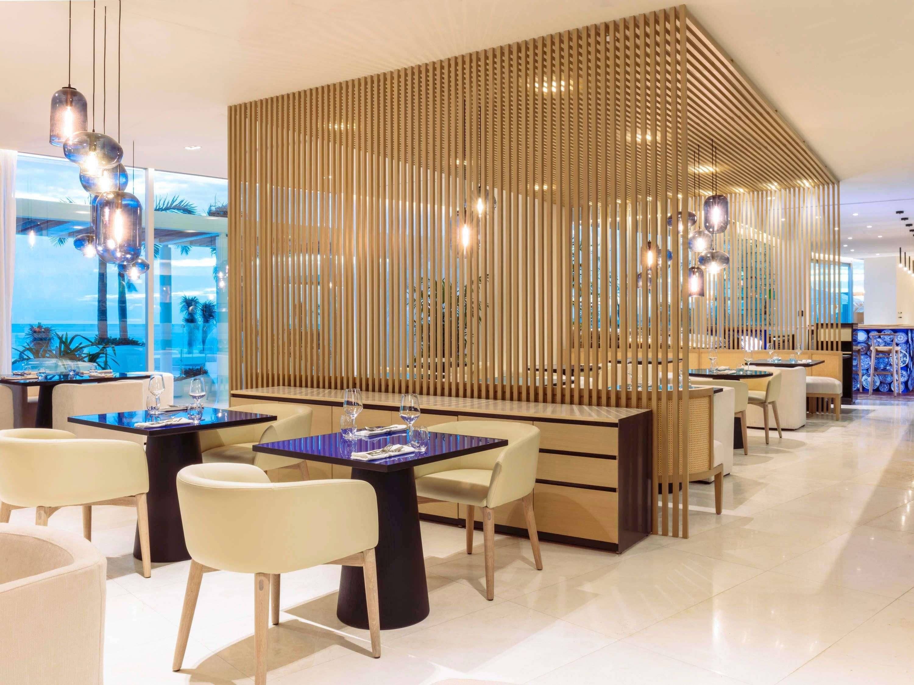 A modern restaurant with a view of the ocean, featuring wooden partitions, contemporary furniture, and pendant lighting.