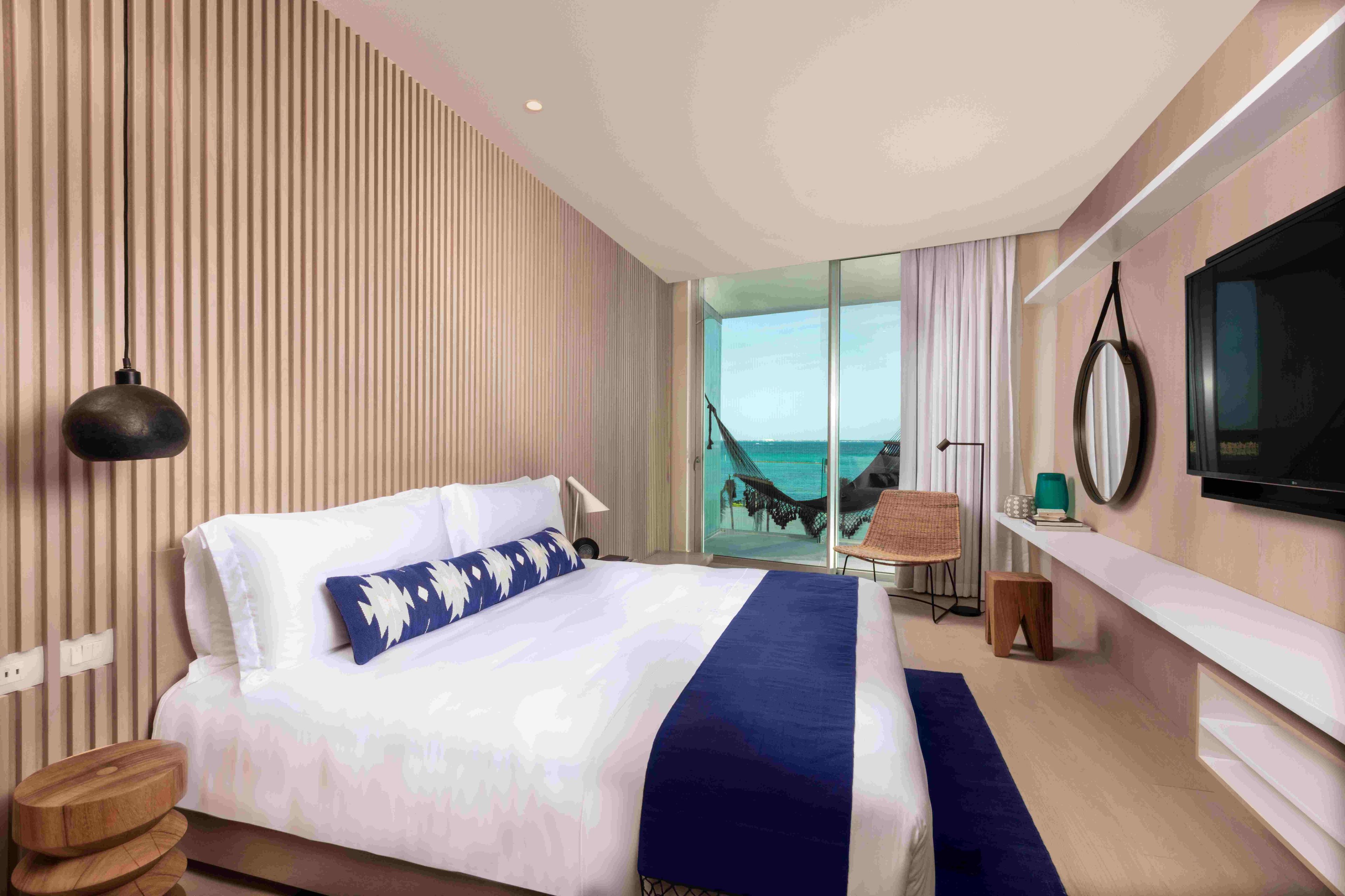 Habitación de hotel moderna con una cama grande, televisión, vista al mar y una hamaca.