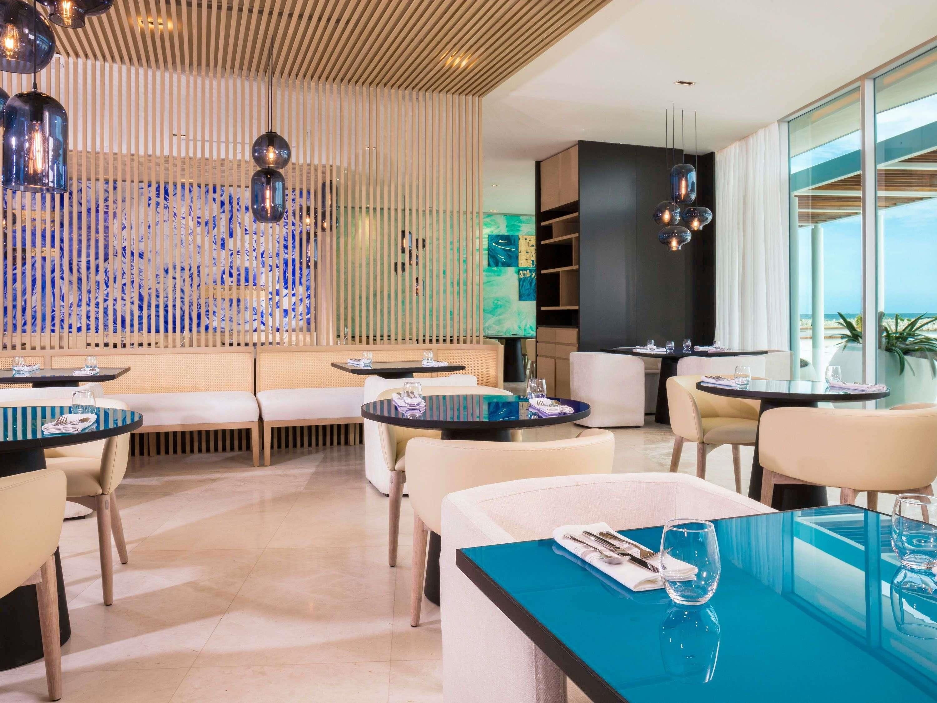 A modern restaurant with round tables, white cushioned seating, and a view of the ocean.