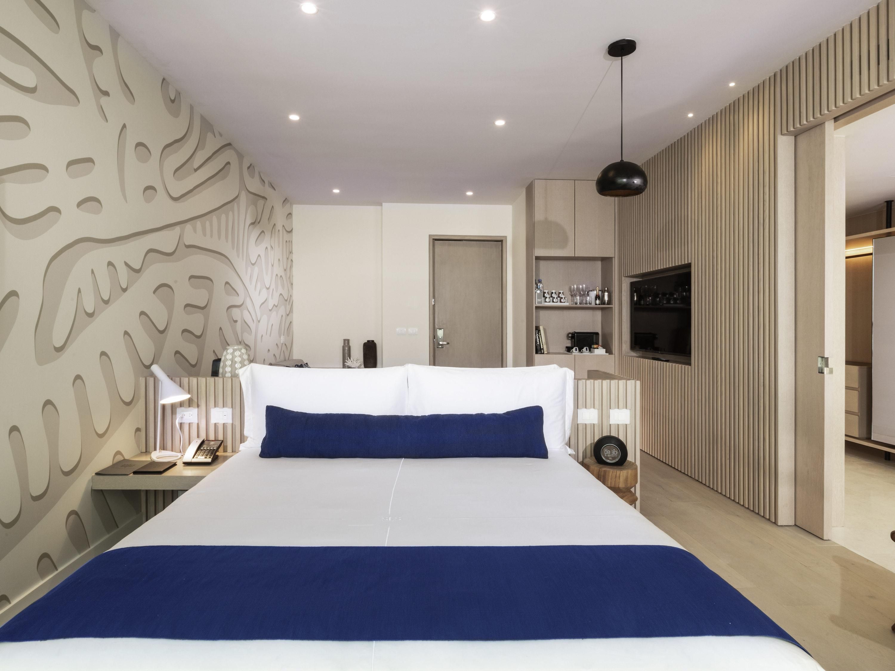 Een moderne slaapkamer met een groot bed, een nachtkastje met een lamp, een televisie en een kledingkast.