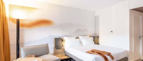 Habitación de hotel con cama, un pequeño sofá, una mesita de noche, una lámpara y un televisor montado en la pared.