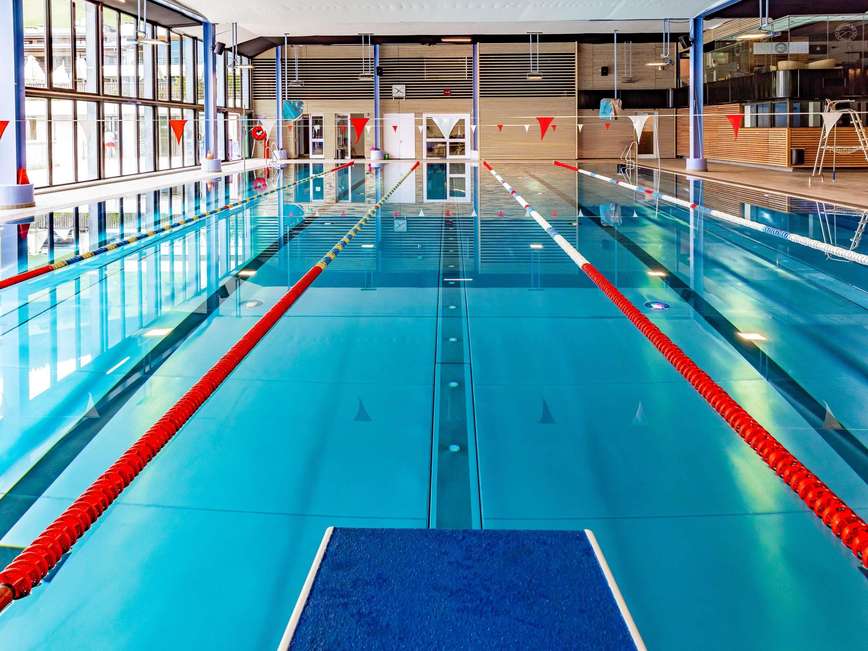 An indoor swimming pool with clear lanes, a diving board, and a changing room area.