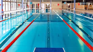 An indoor swimming pool with clear lanes, a diving board, and a changing room area.