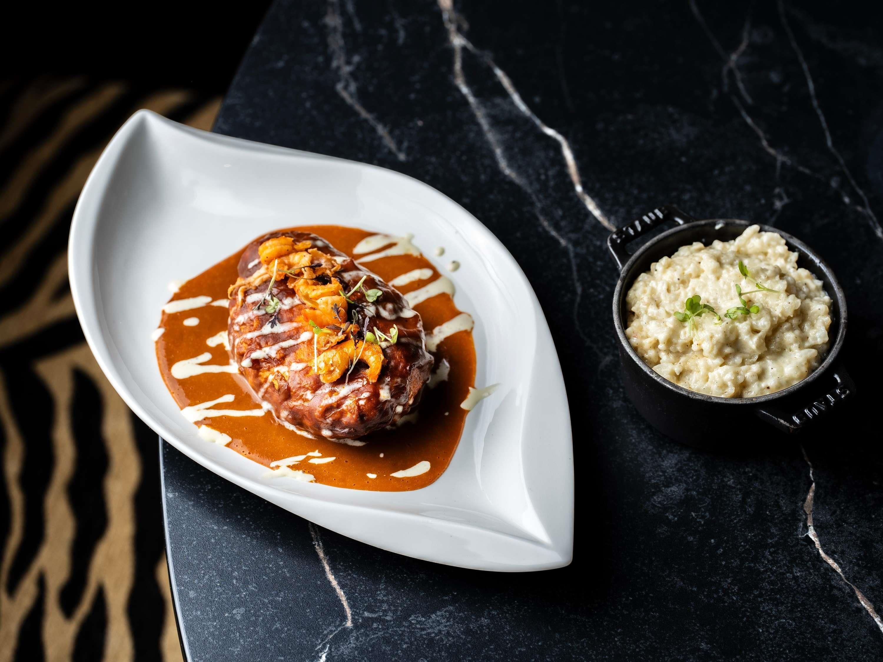 Une assiette blanche contenant un plat de viande et, en accompagnement, un risotto crémeux, le tout posé sur une surface en marbre foncé.