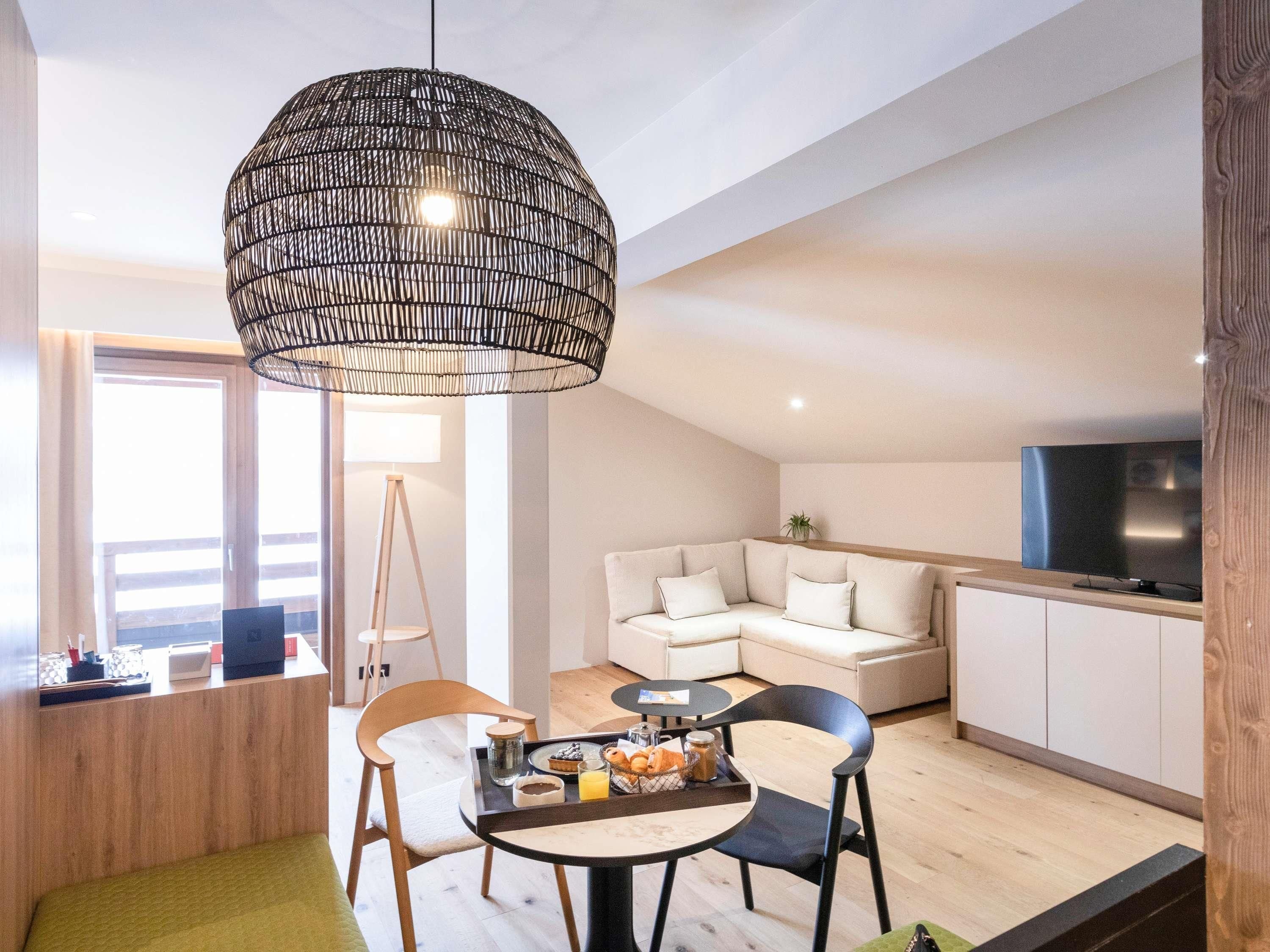 A modern living space with a dining area, a sofa, a television, and a large hanging light fixture.