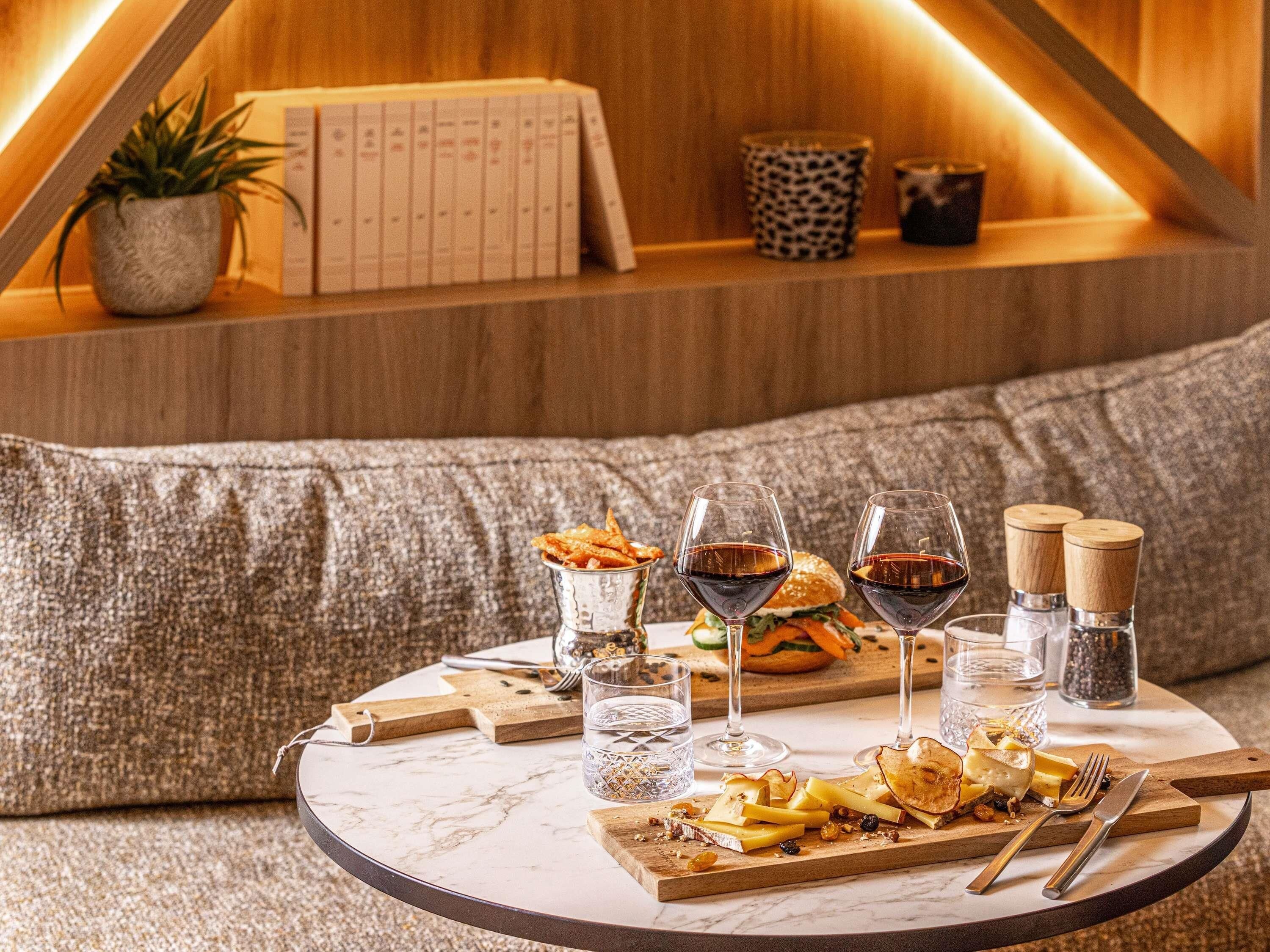 A round marble table with a cheese platter, wine glasses, and cutlery.