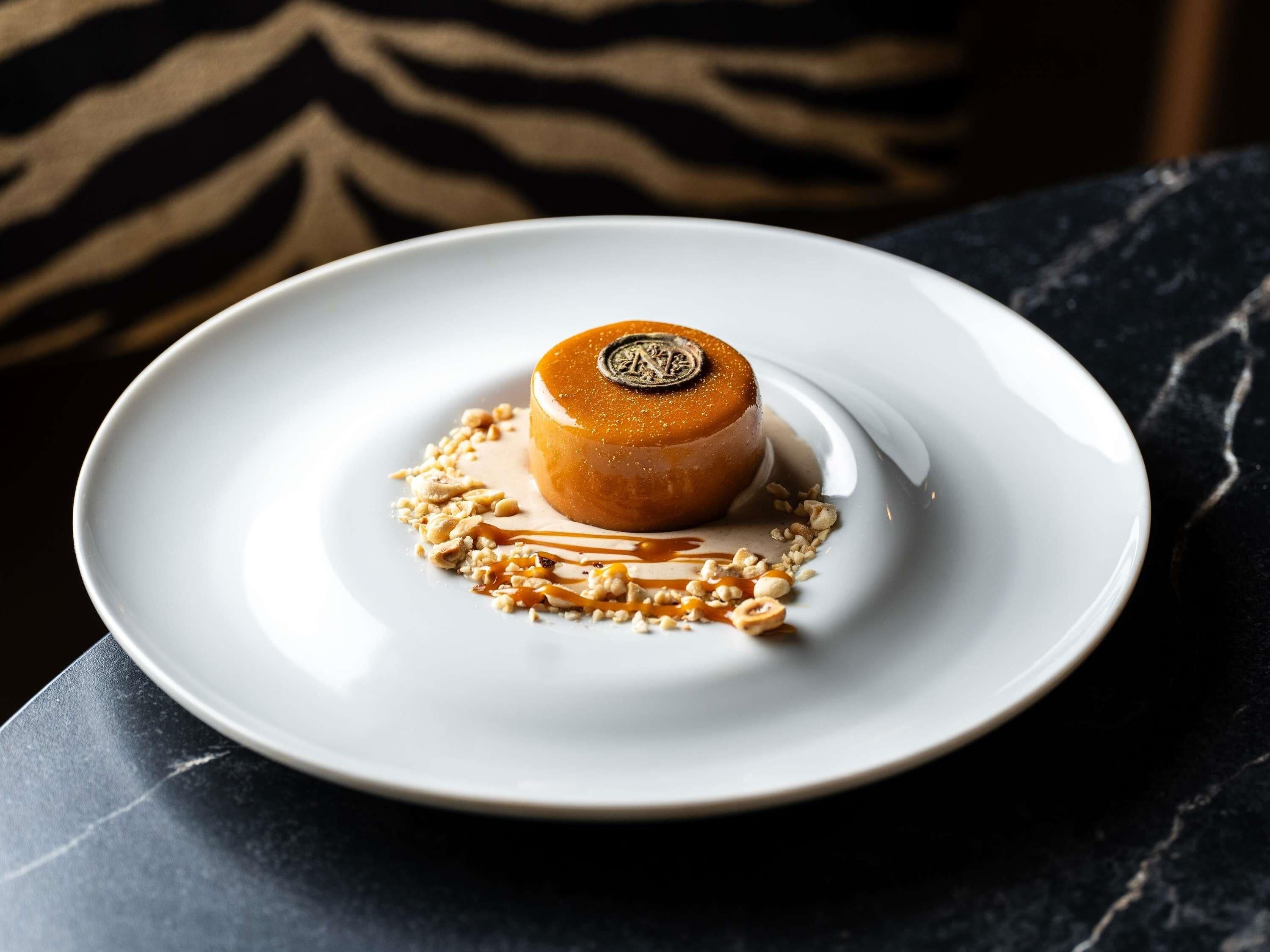 Un postre en un plato blanco con salsa de caramelo y nueces, sobre una superficie oscura.