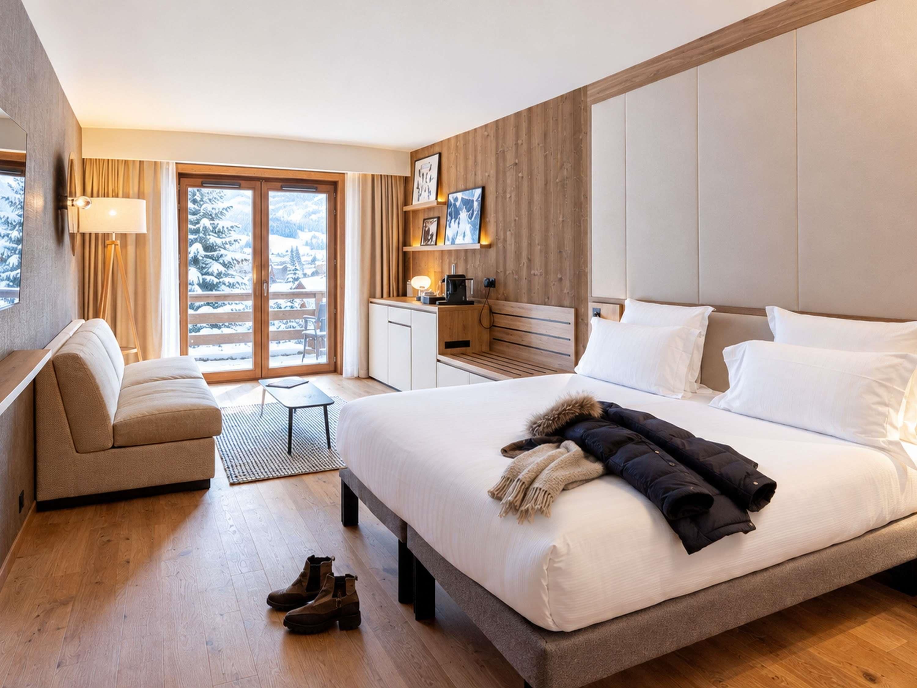 A hotel room with a large bed, a sofa, a desk, and a view of a snowy landscape.