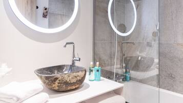 Un bagno moderno con uno specchio rotondo, un lavabo in pietra e una cabina doccia in vetro.