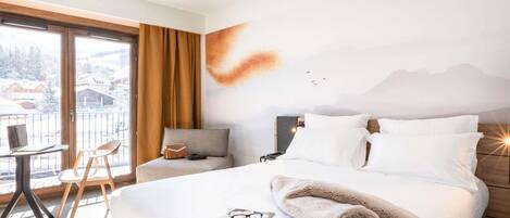 A hotel room with a bed, a desk, a chair, a view of the outside, and a wall with a mountain painting.